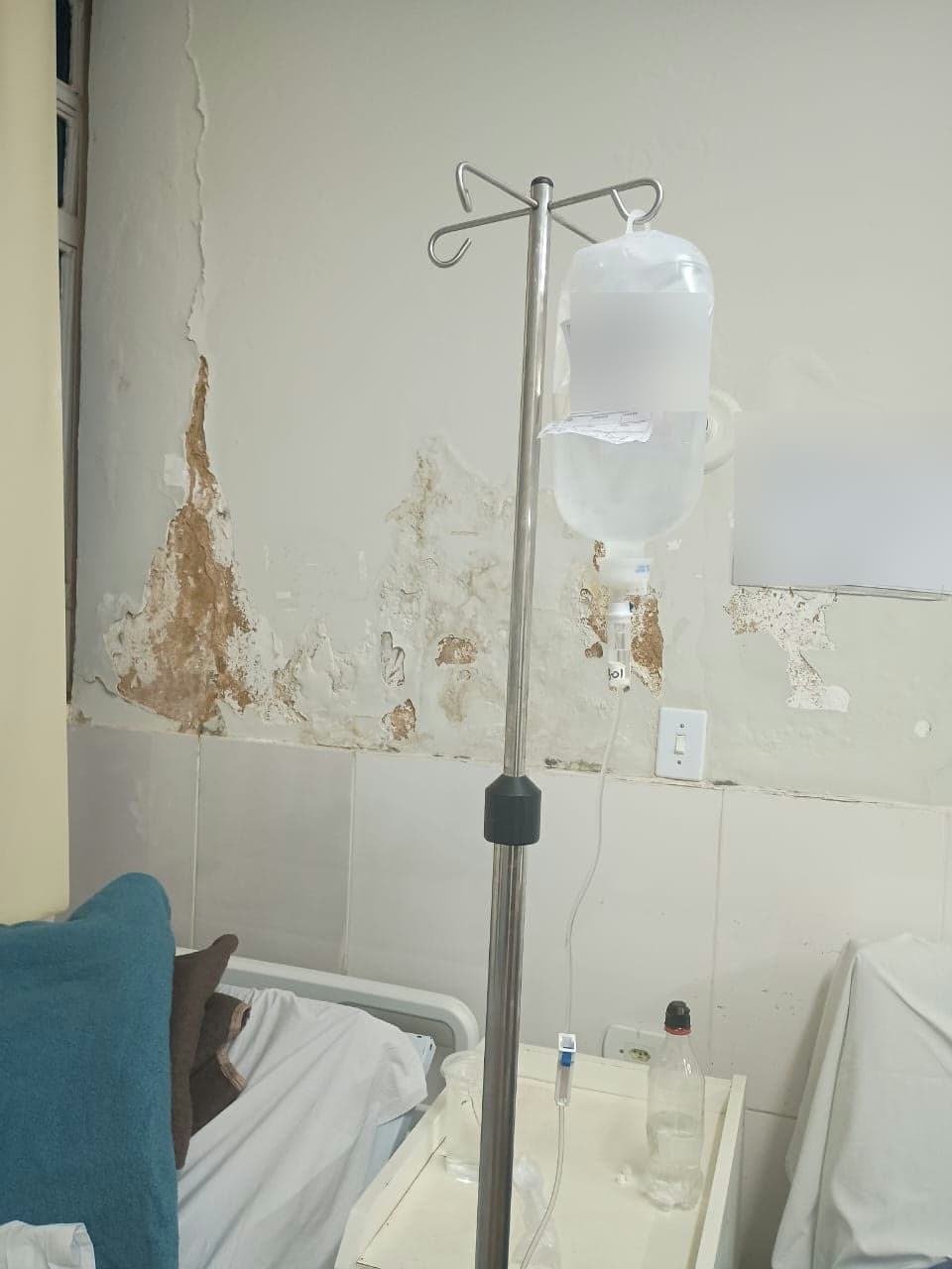 Suporte de soro em enfermaria, parede com infiltração e mofo ao fundo