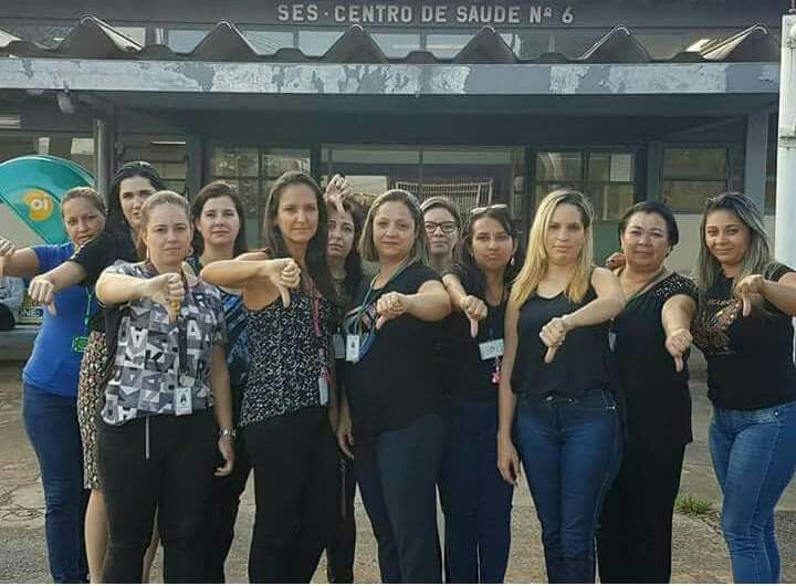 Grupo de servidoras de saúde em protesto, sinal de reprovação, em frente a centro de saúde